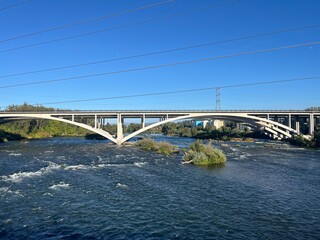 Beautiful arch bridge crossing a wide river under a clear blue sky with power lines in the background