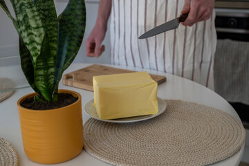 human hand cutting butter on a wooden board in the kitchen at home