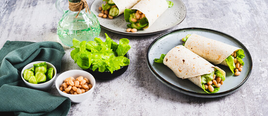 Tortilla wraps with cucumber, white beans and lettuce on a plate on a table web banner