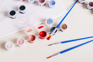 Brush dipped in red acrylic paint and containers with paints for painting a picture