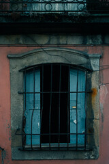 Obraz premium An old window with bars on the facade of a worn building.