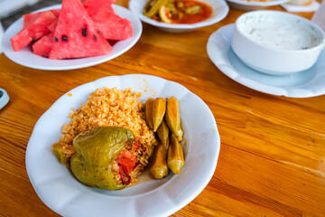 Turkish handmade food on a table. Eating simple food. Rise or bulgur with okra, and stuffed pepper. Yoghurt or dzadziki and slices of watermelon
