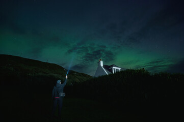 Northern lights and a man looking at sky standing at house. Isle of Skye, Scotland 
