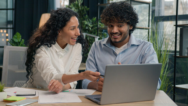 Multiracial business partners happy diverse colleagues Indian businessman and Arabian businesswoman win online project on laptop achievement happy office team workers employees celebrate success deal