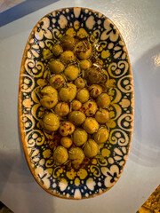 Green olives in olive oil. Charming Turkish style ceramic plate directly above. Tiny olives in marination
