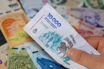 Argentina money, 10,000 Argentine pesos banknote held in hand against the background of other denominations, close up