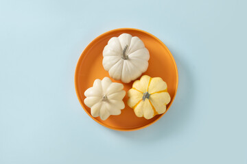 Autumn concept with three pumpkins in seasonal orange plate on blue background. View from above. Thanksgiving Day sale concept.