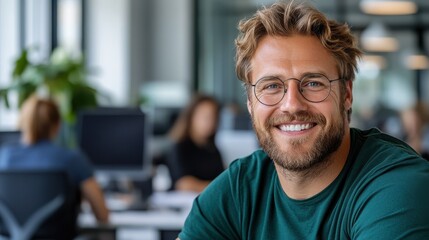 Fototapeta premium A bearded man with glasses showing a bright smile sits in a lively office space filled with colleagues, depicting a friendly and energetic work atmosphere.