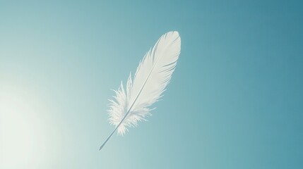Obraz premium A white feather drifting against a clear blue sky with the golden sun overhead