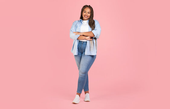 Attractive African American Female Posing Wearing Plus Size Clothes, Standing Crossing Hands And Smiling To Camera On Pink Background In Studio. Body Positive Concept. Full Length Shot