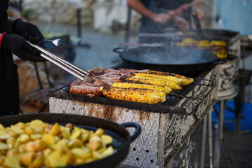 Man grilling sausages and corn on the grill. Street helthy vegetarian food.