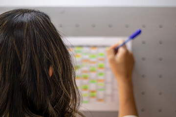Back of Female office worker writing with ballpoint pen on color-coded wall calendar