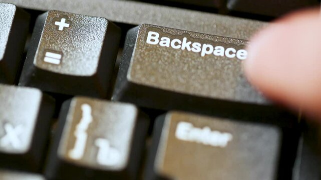 Computer user finger pressing backspace button on modern black computer keyboard.