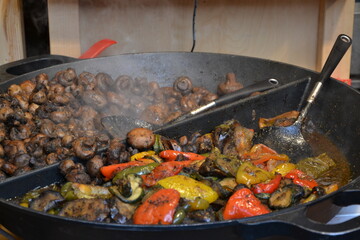 Grande casserole dans laquelle est cuisinée des légumes, poivrons rouges et verts et des champignons