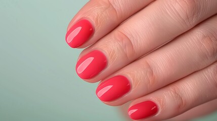 Bright coral pink manicure on female nails against a mint green background, providing copy space for nail art visuals, beauty themes, or summer marketing, ideal for salons or nail products.

