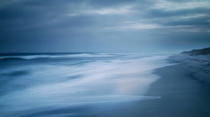 Fototapeta premium A long exposure photograph of the beach. The ocean is calm and blue, with some fog on top