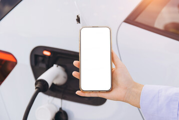 Smartphone Display Held in Hand Beside Charging Electric Car Symbolizes Technology and...
