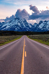 Fototapeta premium Lonely Road Leading to Majestic Grand Teton Mountains at Sunset