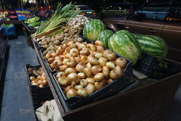 Night fruit and vegetable market. Crates filled with fresh products. Onions, watermelons, green onions, and potatoes. Vibrant street market atmosphere. Local grocery store background.