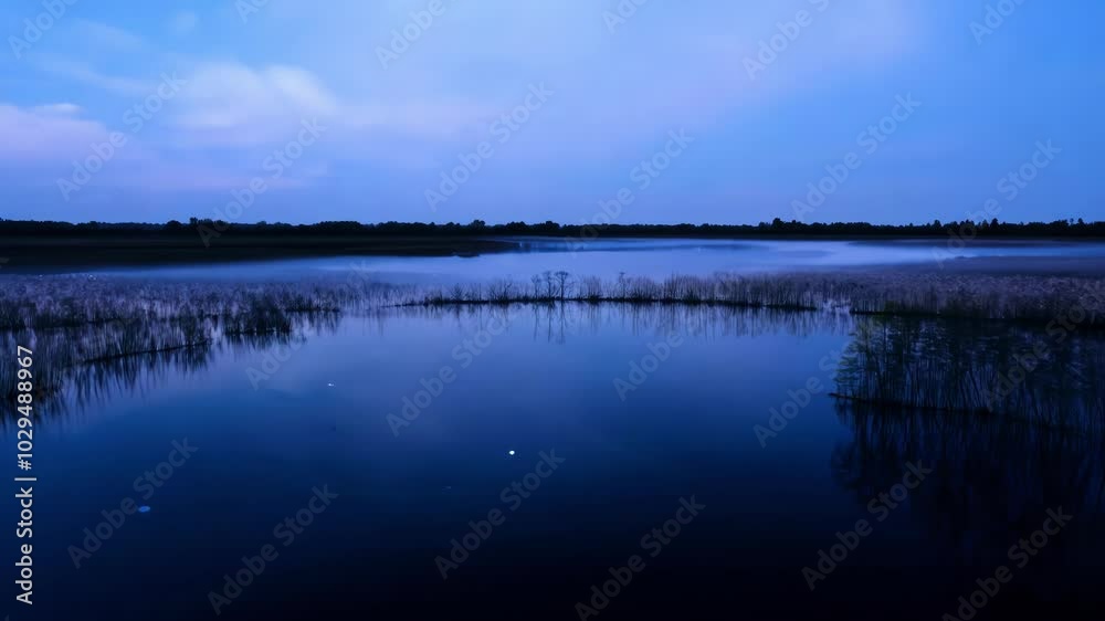 Aufkleber Tranquil lake reflects the twilight sky, with reeds adding to the beauty of the landscape, creating a serene and peaceful atmosphere under a calming blue evening sky