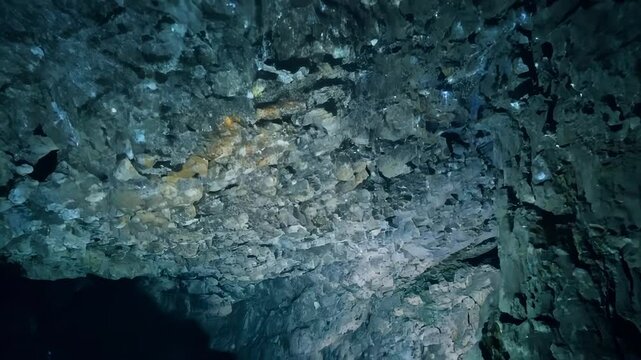 Beam of light illuminates the rocky ceiling of an underwater cave, revealing the rough texture and intricate details of the geological formations
