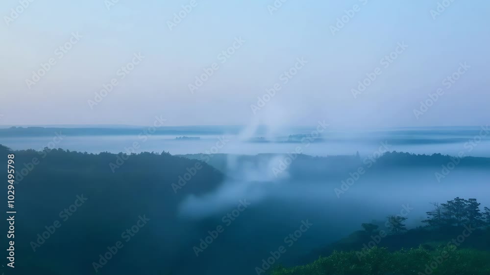 Poster Layers of fog are hovering over a valley filled with forest, creating a mysterious landscape illuminated by the soft light of dawn
