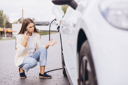 Worried Woman Charging Electric Car and Making Phone Call