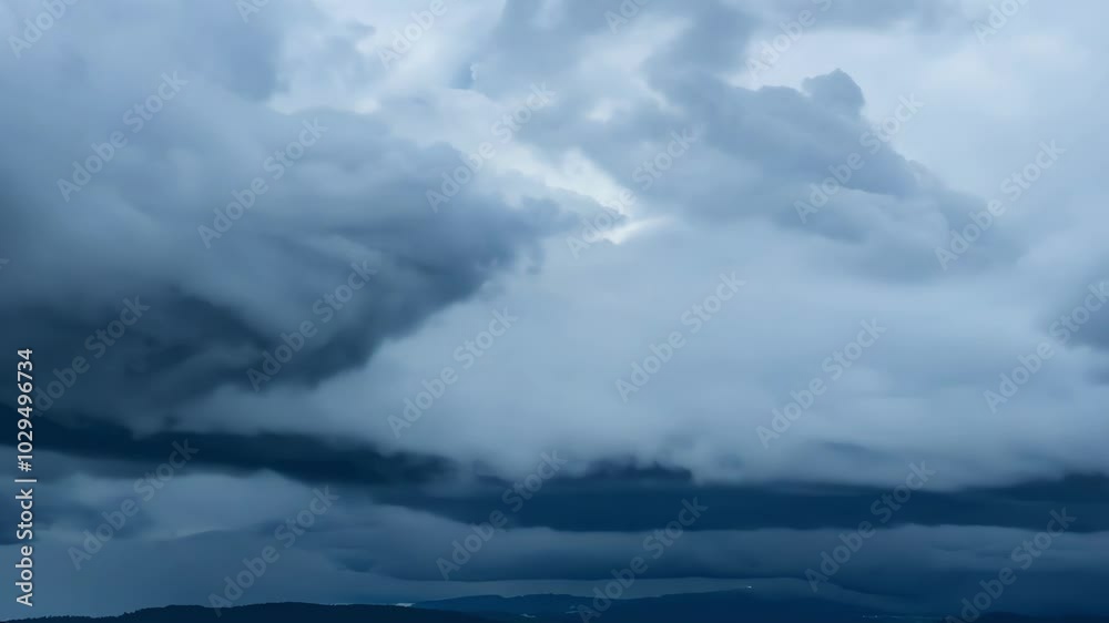 Poster Dark storm clouds are gathering over a mountain range, creating a dramatic and ominous sky. The clouds are heavy with rain, and the air is thick with humidity