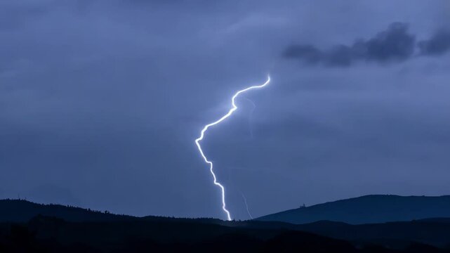 Bright bolt of lightning striking in the distance, illuminating the night sky and the silhouette of a mountain range below