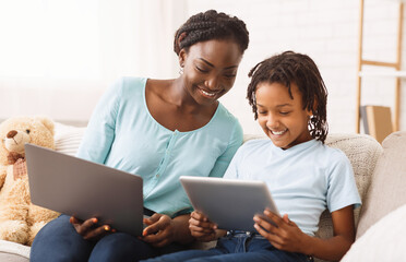 Black Mother Helping Daughter With Homework, Studying Together Using Digital Tablet And Laptop