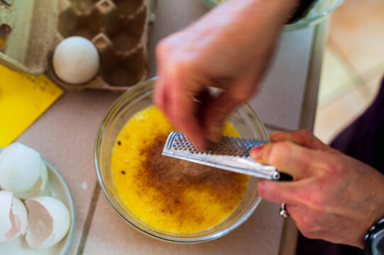 A woman's hands grating nutmeg onto an egg mixture in a bowl
