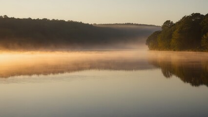 Obraz premium A gentle fog blankets a peaceful river at sunrise, with warm sunlight reflecting off the mist and water. The soft fog over the water and the lush green banks create a serene and atmospheric rural scen