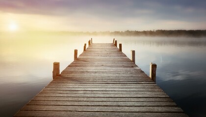 Obraz premium A weathered wooden pier extending into a calm misty lake, with soft light reflecting off the 