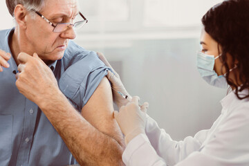 Obraz premium Flu Vaccine. Close up of young latina nurse giving elderly male patient injection in hospital room, copyspace