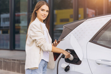 Young Woman Charging Electric Car at Modern Charging Station