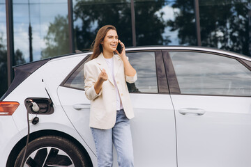 Confident Woman Using Smartphone Near Electric Car Charging Station