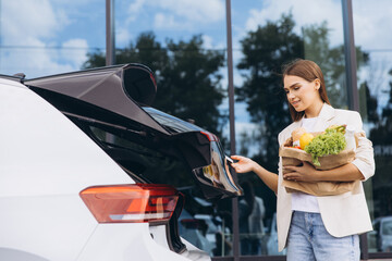 Young Woman Unloading Groceries from Car Trunk in Urban Setting