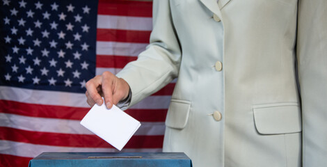 Hand placing vote in ballot box with USA flag in background  election concept