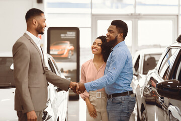 Fototapeta premium Car Dealer Handshaking With Happy Auto Buyers After Successful Deal In Dealership Store. Selective Focus
