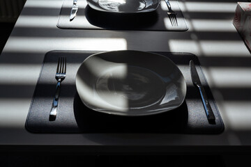 A white table with dark blue place mats, two plates, cutlery, and a box of tissues. Sunlight from...
