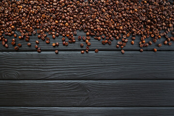 Fototapeta premium Coffee beans scattered on dark wooden surface. A top-down view of roasted coffee beans spread across a dark textured wooden surface.
