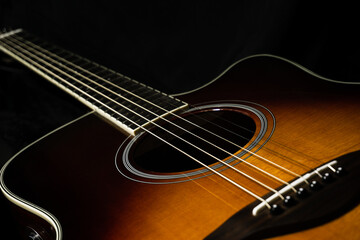 Acoustic guitar on black background, sunbrust body acoustic guitar parts close up,  plucked instrument, shallow depth of field part of a acoustic guitar, guitar chords, playing music