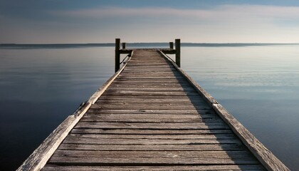  Worn-out wooden pier stretching over still waters, with subtle shadows of the weathered boar