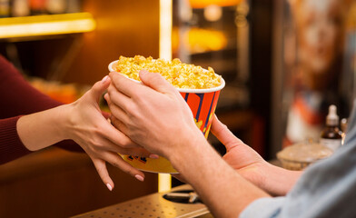 Cinema and entertainment. Young man buying popcorn from saleswoman in movie theater lobby, closeup...