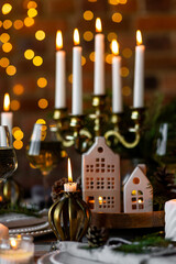 Beautiful table setting for family Christmas dinner at home. Cozy atmosphere, candlelight. Wine glasses, vintage chandelier, elegant interior. Fir tree branches, wooden furniture, dark, bokeh