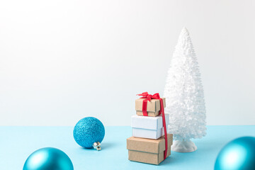 Snowy Christmas tree with Christmas decoration and gift boxes on blue table. Christmas or New Year minimal concept.