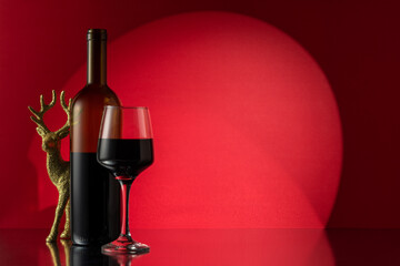 Christmas reindeer with red wine bottle and glass of wine on red wall background. New Year or Christmas concept.
