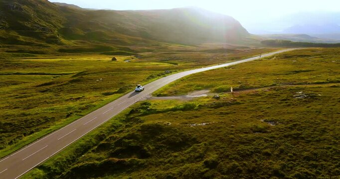 White electro car travelling through cinematic scenery with epic Scottish hills and bright blue sky on sunny day