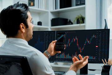Trader businessman searching on smartphone, analyzing in dynamic stock exchange investment screen on pc with invest highest profitable financial technology market at modern home office. Surmise.