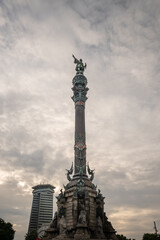 Monumental structure featuring a statue atop a tall column in a cityscape during cloudy twilight hours